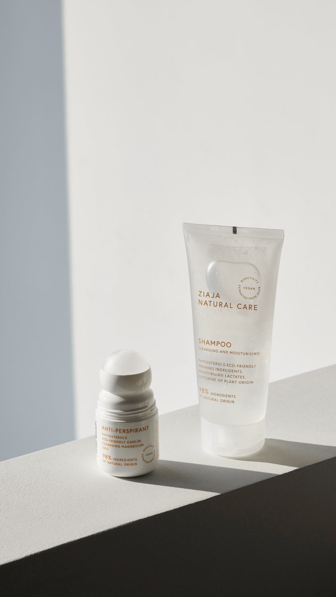 Ziaja Natural Care shampoo tube and roll-on anti-perspirant displayed on a light pedestal, photographed in soft daylight with minimal shadows on a clean background.