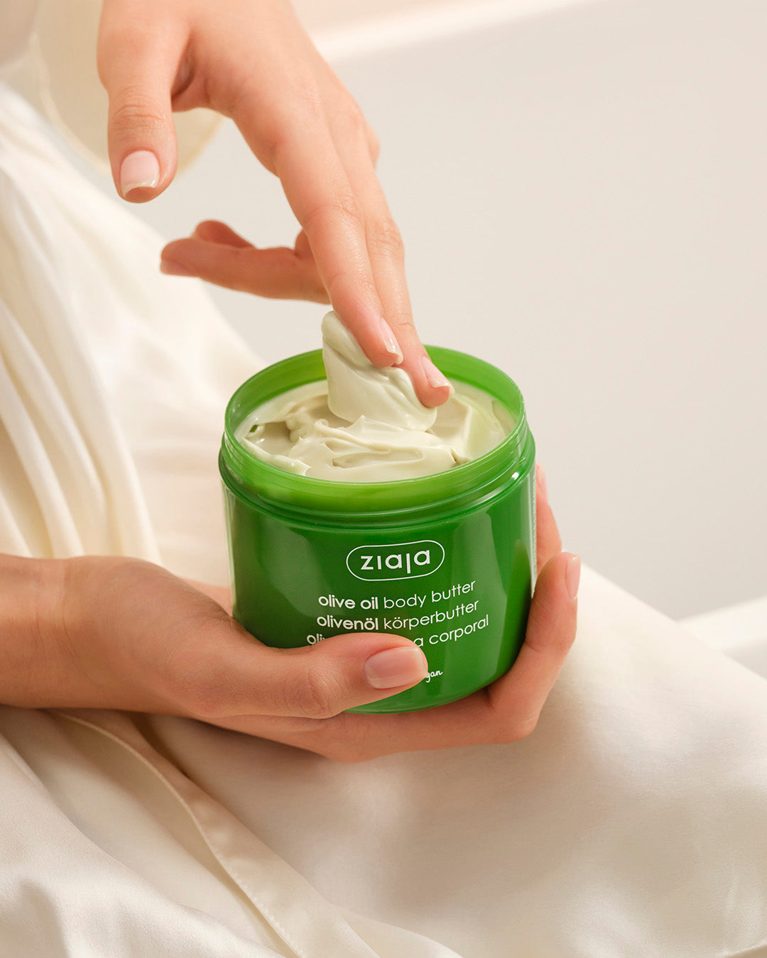 Person using Ziaja olive oil body butter from a green jar.