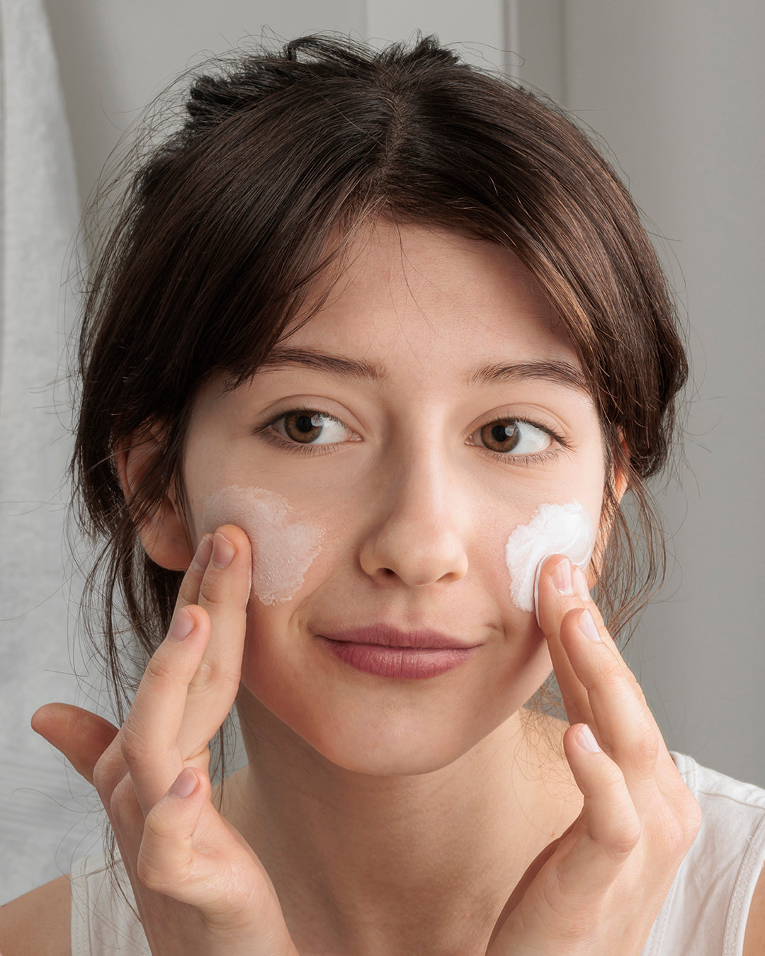 Woman applying cream to her face with a neutral background