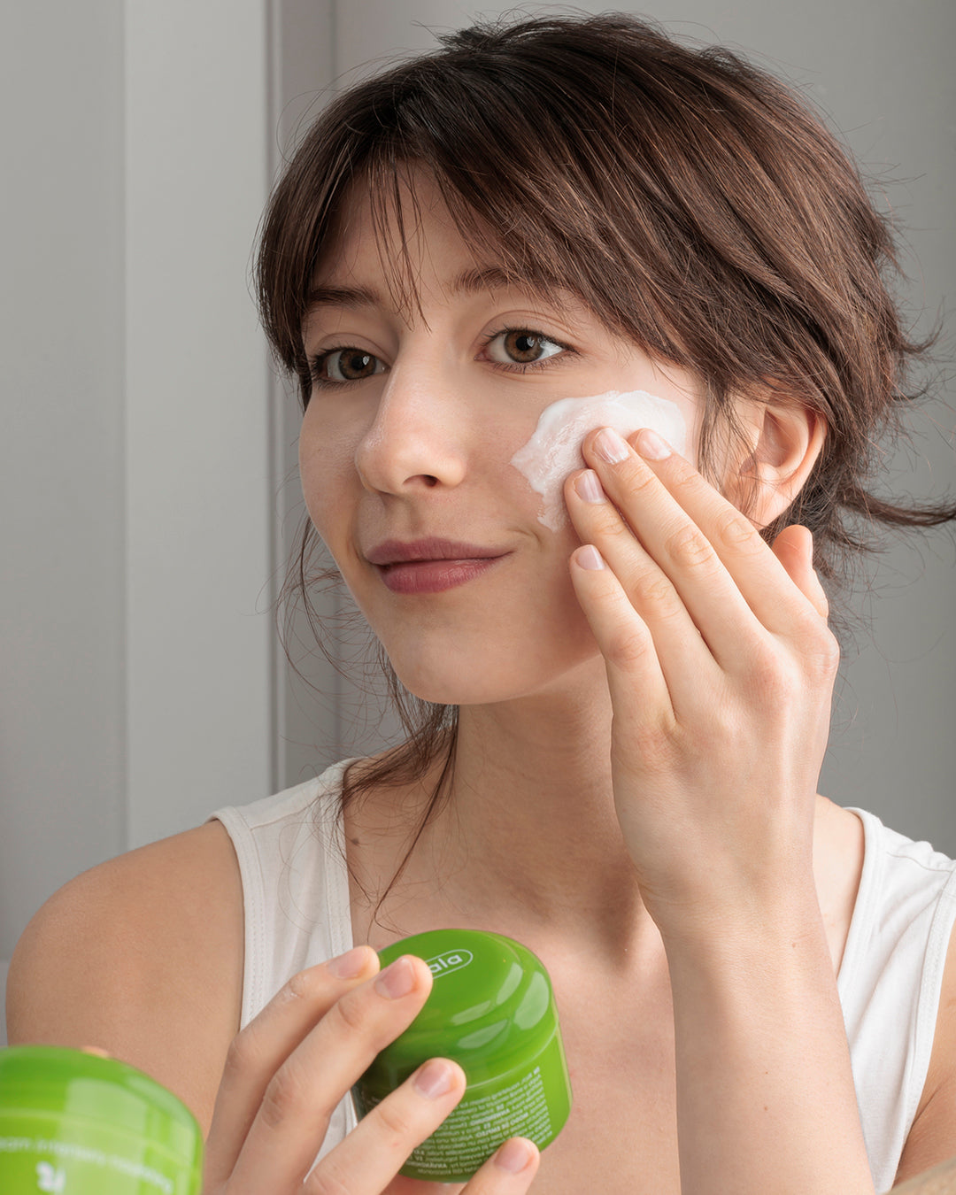 Woman applying Ziaja olive cream to her face with a green container in hand