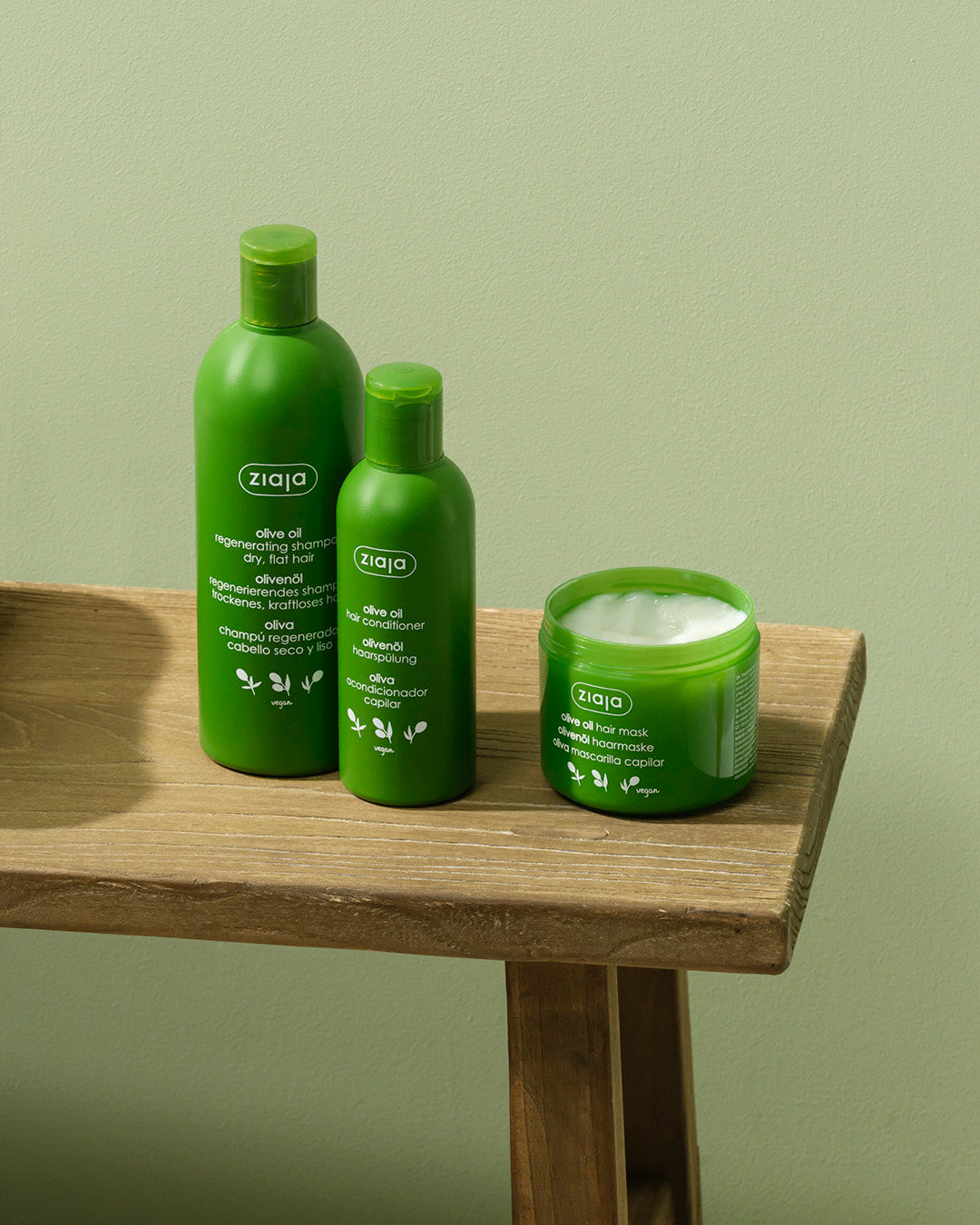 Three green bottles and a jar of Ziaja products on a wooden surface with a green background.