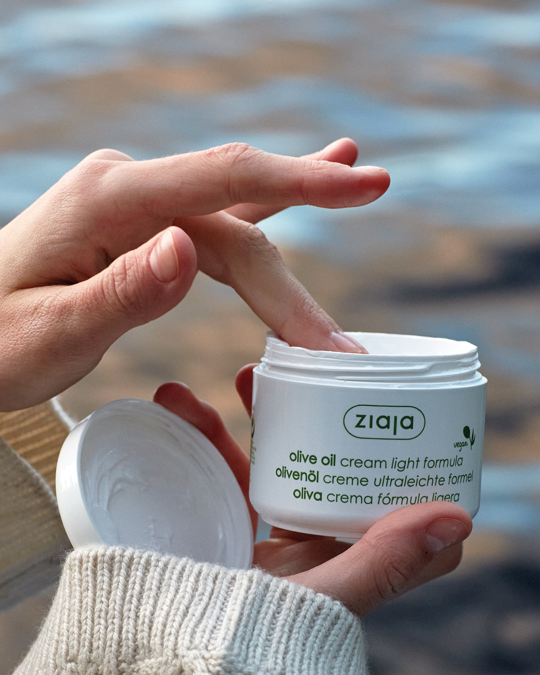 Person applying Ziaja olive oil cream to their hand with a blurred background