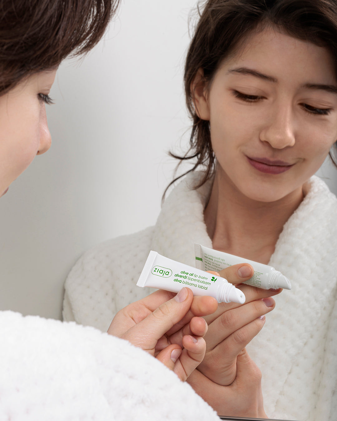 women examining a tube of Ziaja olive oil lip balm with a neutral background