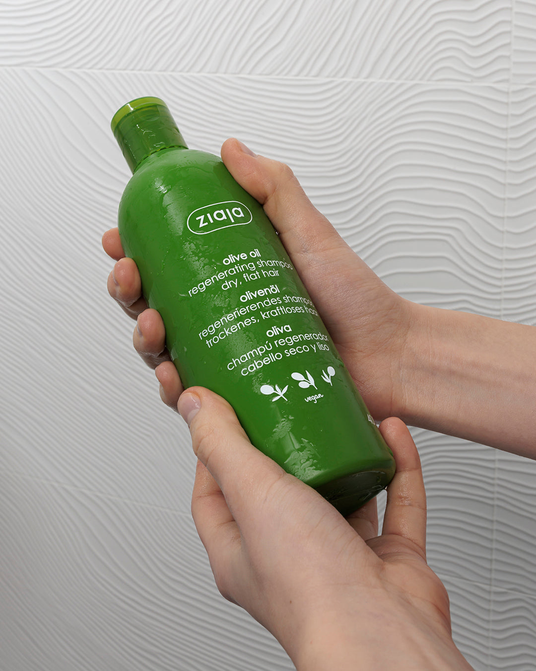 Ziaja olive oil Green shampoo bottle held by a hand against a white background