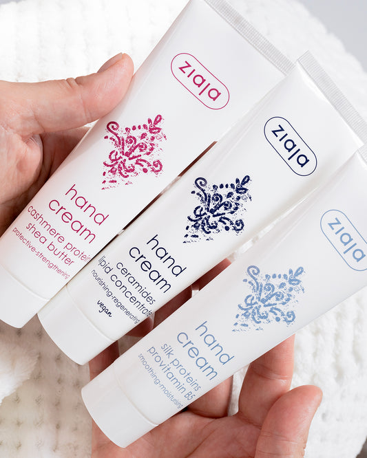 Hands holding three Ziaja hand creams—Cashmere (pink), Ceramides with lipid concentrate (navy), and Silk Proteins with provitamin B5 (light blue) in white tubes.