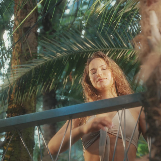 A video showing a woman spraying Ziaja Tropical Citrus mist on palm trees background.