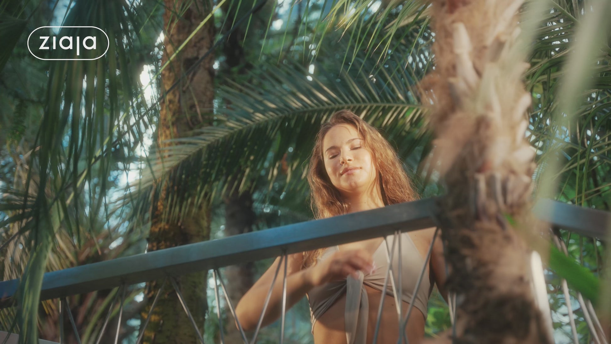 A video showing a woman spraying Ziaja Tropical Citrus mist on palm trees background.