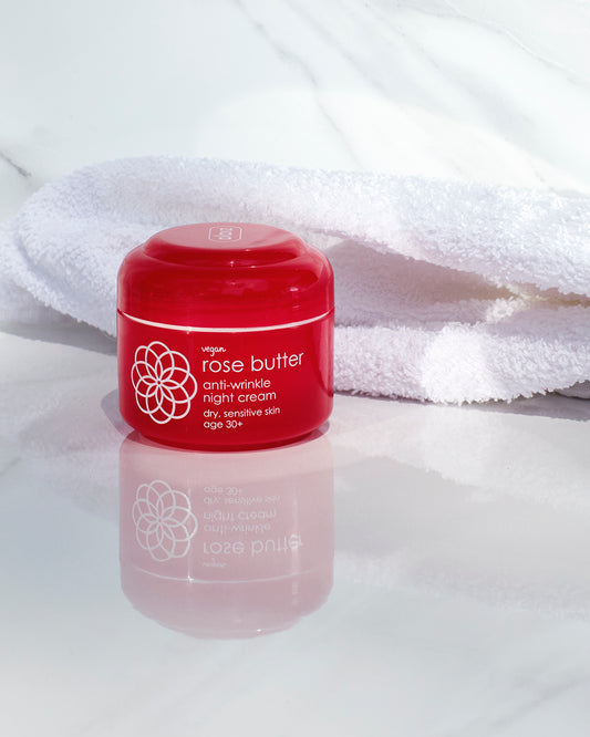 Red jar of rose butter anti-wrinkle night cream on a white surface with a white towel in the background.