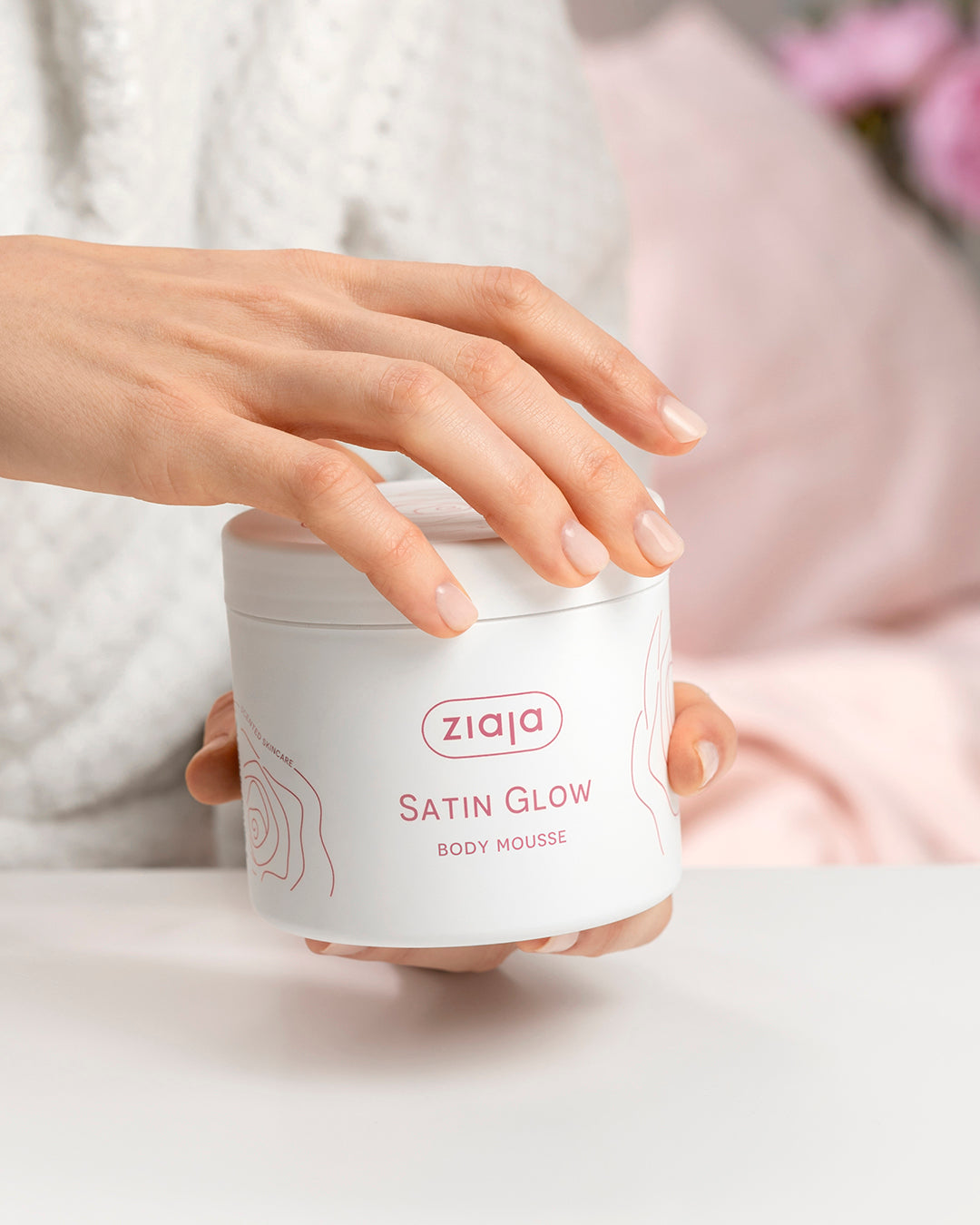 Person holding a Ziaja Satin Glow body mousse container with a blurred background