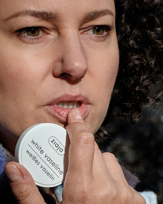 Person applying lip balm while holding Ziaja White Vaseline tin (close-up).