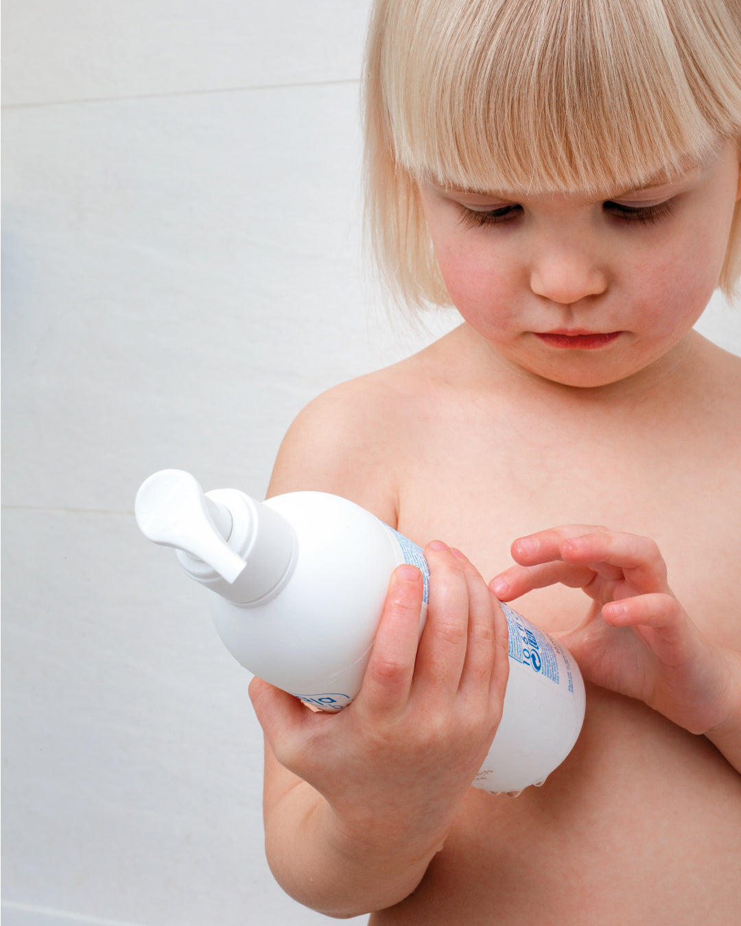 Toddler holding and looking at a bottle of Ziaja Baby body & hair shower gel in the bathroom.