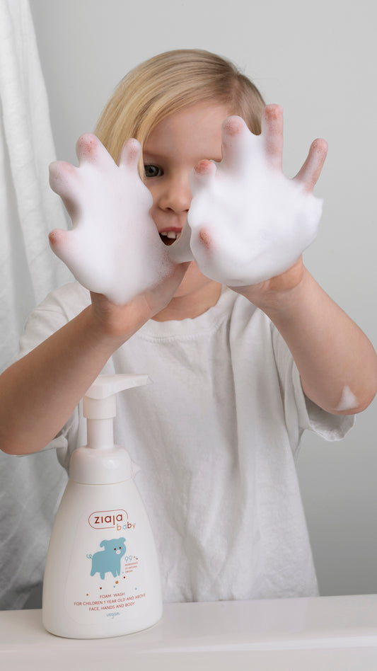 Child playing with foam on hands next to Ziaja Baby Foam Wash pump bottle (for children 1 year old and above
