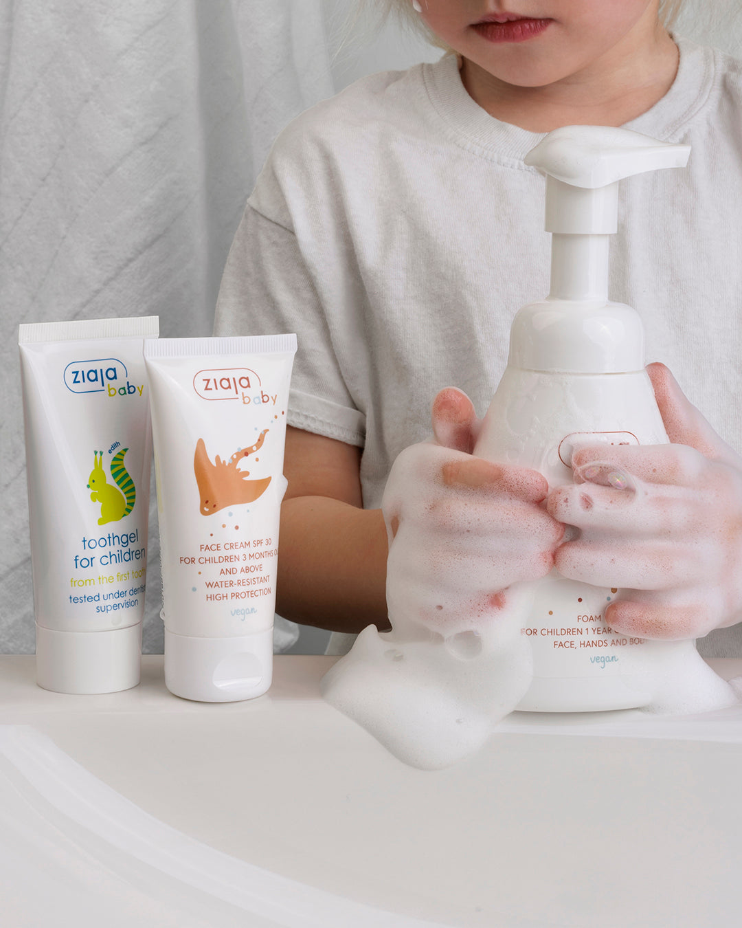 Child washing hands with Ziaja Baby Foam Wash next to Ziaja Baby Face Cream SPF 30 Water Resistant and Ziaja Baby Toothgel for Children.