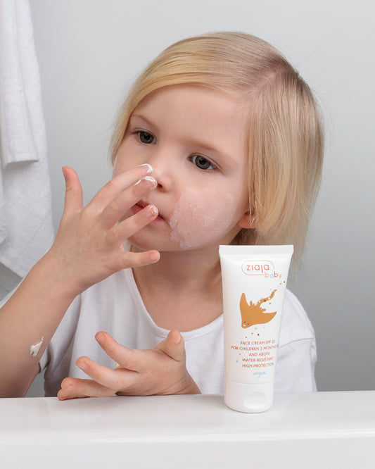 Child applying Ziaja Baby Face Cream SPF 30 Water Resistant, with the product tube on the counter