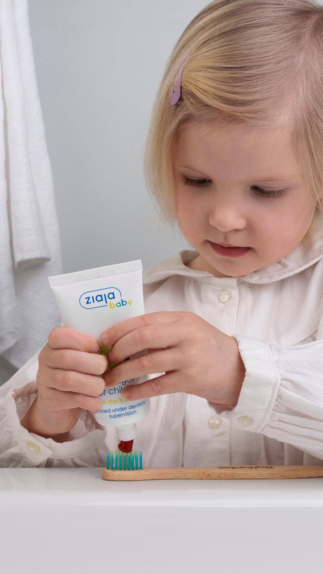 Child applying Ziaja Baby Toothgel for Children (fluoride-free) onto a toothbrush.