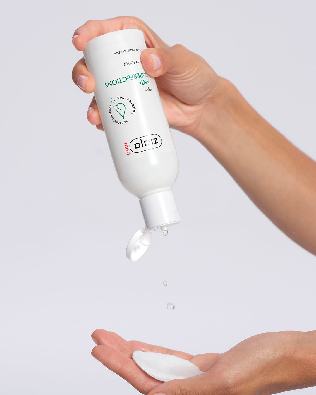 Hand holding a white bottle labeled 'Ziaja Med Anti-imperfections face toner' with product being dispensed onto the palm against a light gray background