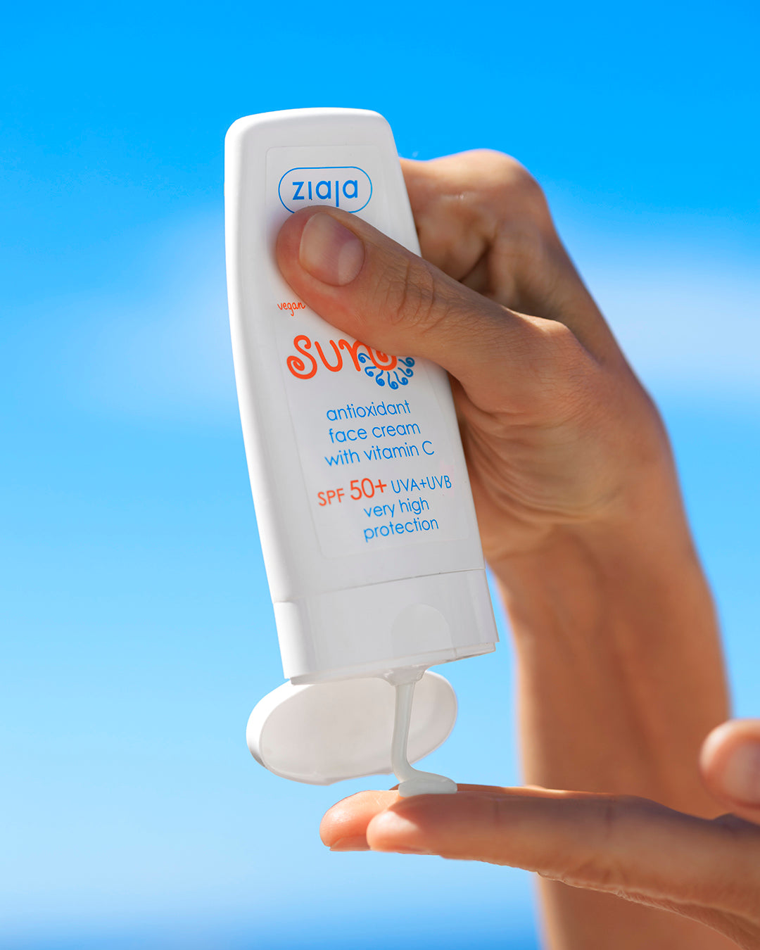 Hand holding a Ziaja Sun suncream against a blue sky background