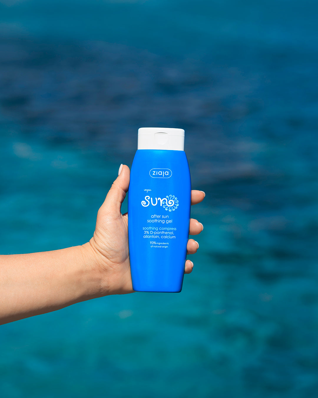 Hand holding Ziaja Sun After Sun Soothing Gel bottle with sea in the background